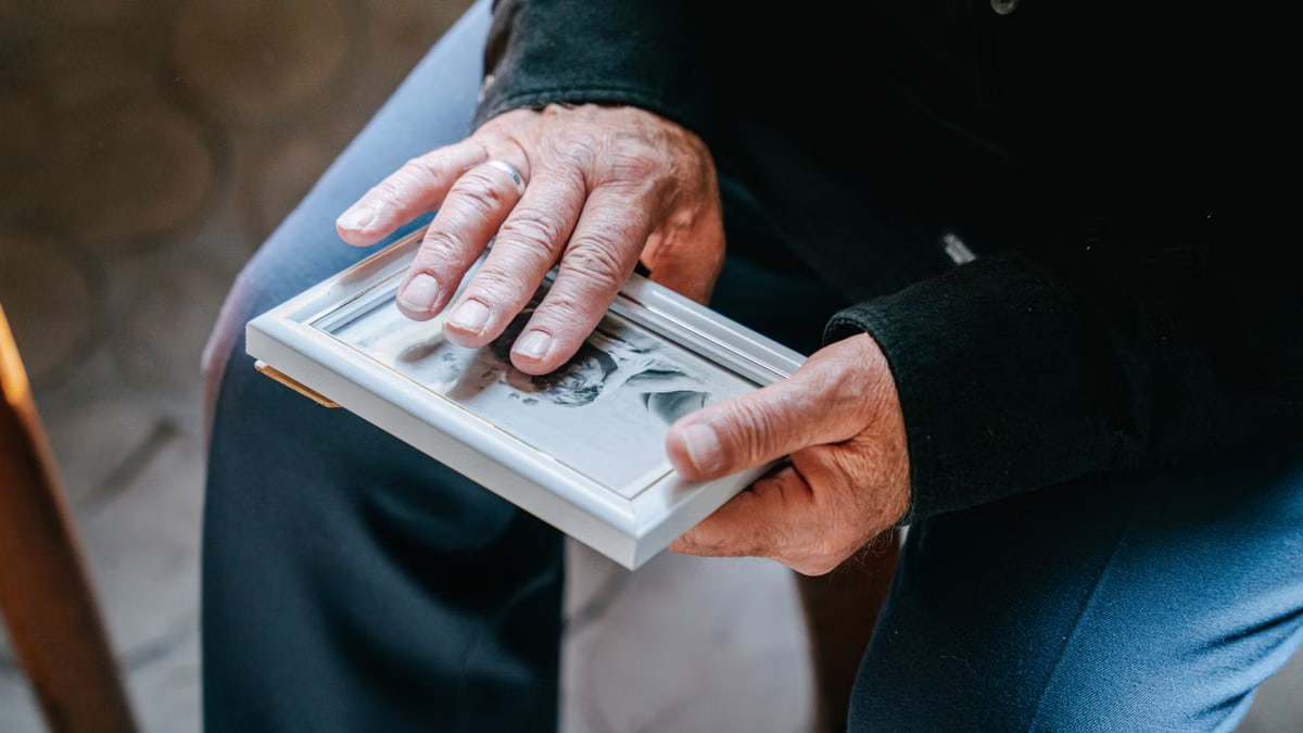 Close-up of elderly hands holding a framed photograph, reflecting nostalgia and emotion.