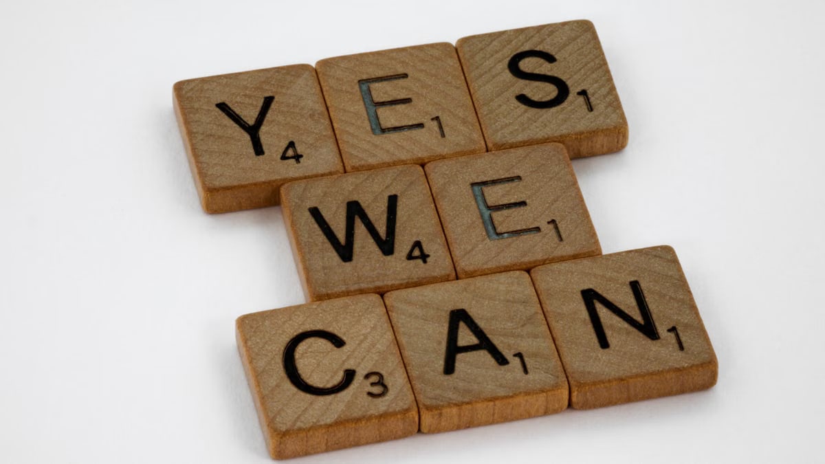 Wooden Scrabble tiles arranged to spell 'Yes We Can', emphasizing motivation on a white backdrop.